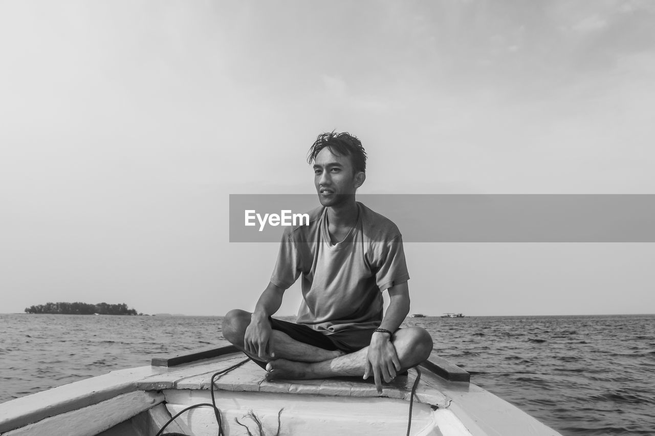 Young man sitting on boat in sea against sky