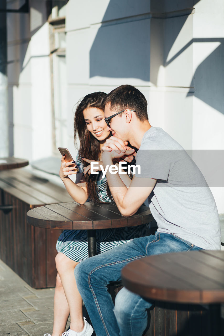 Smiling couple using mobile phone at outdoor cafe