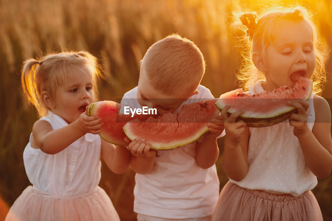 Cute kids eating watermelon during sunset outdoors