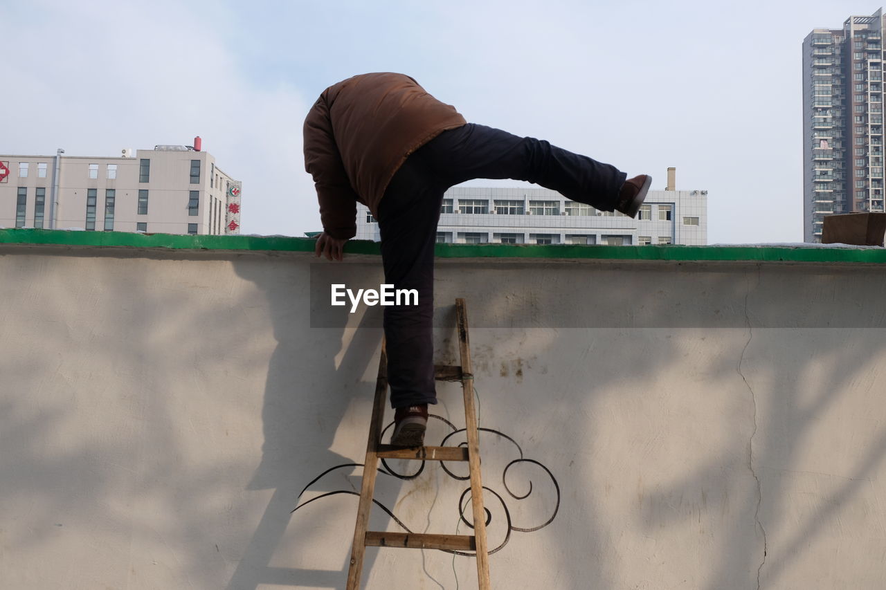 Low angle view of man climbing on wall with help of ladder