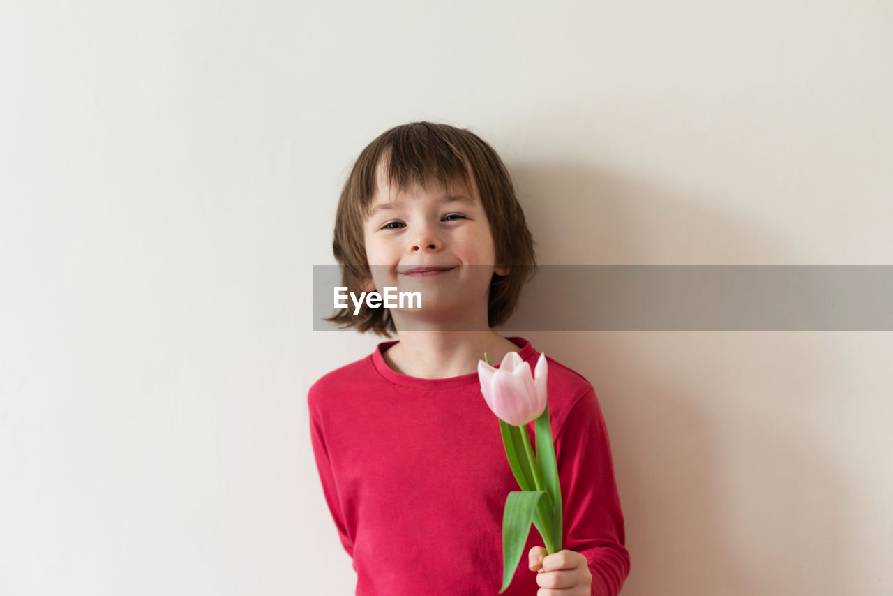 childhood, child, one person, portrait, pink, smiling, indoors, happiness, emotion, studio shot, looking at camera, women, white background, female, waist up, copy space, front view, red, clothing, person, cute, flower, brown hair, hairstyle, innocence, casual clothing, cheerful, standing, positive emotion, holding, toddler, photo shoot, headshot