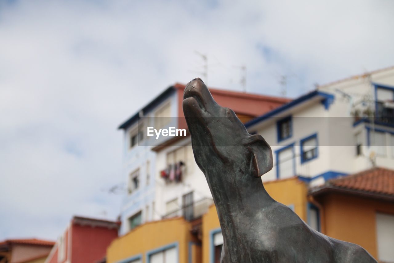 Low angle view of dog statue by building against sky