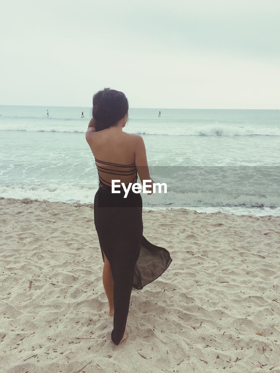 Rear view of young woman on shore looking at sea against clear sky