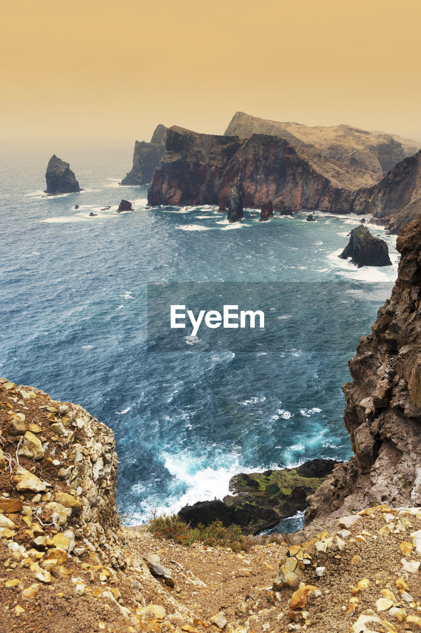 High angle view of rocky coastal feature against clouds