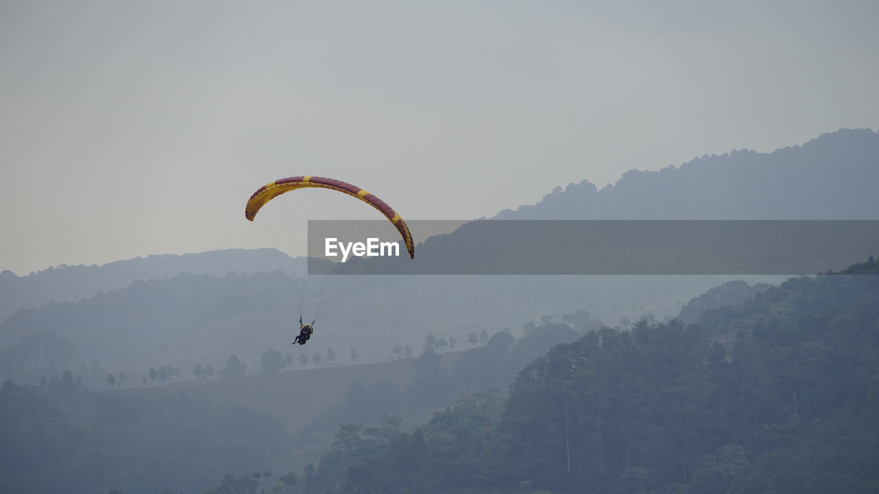 PERSON PARAGLIDING AGAINST MOUNTAIN RANGE