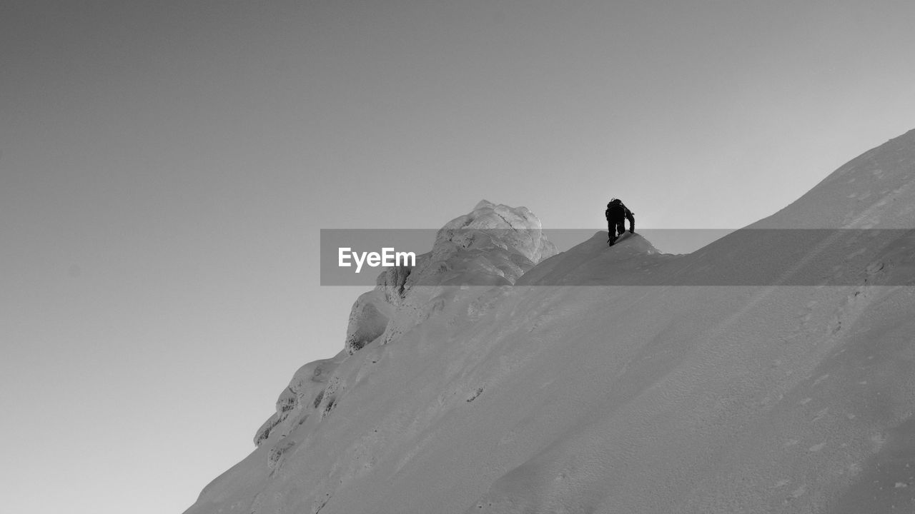 LOW ANGLE VIEW OF PERSON ON SNOW COVERED MOUNTAIN AGAINST CLEAR SKY