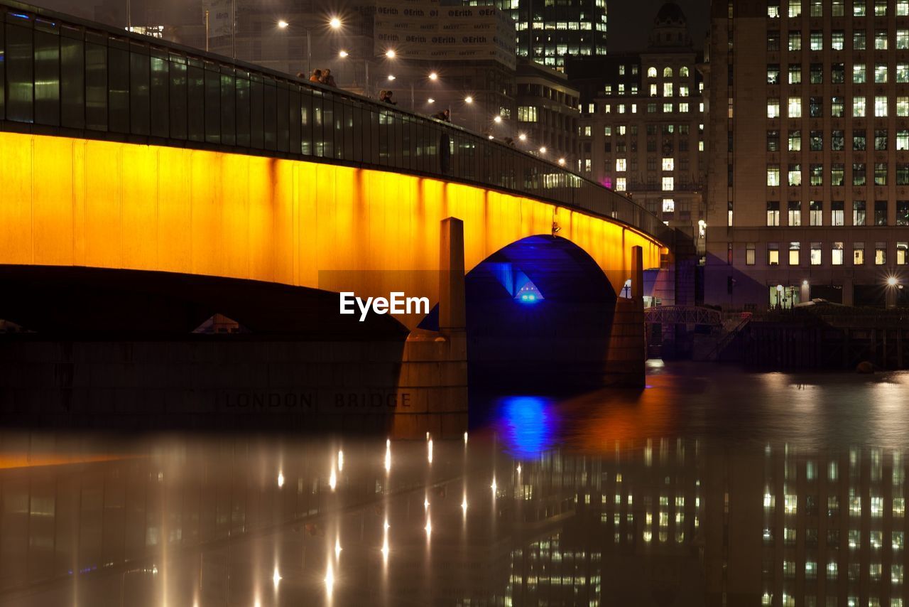 Illuminated arch bridge over river in city at night