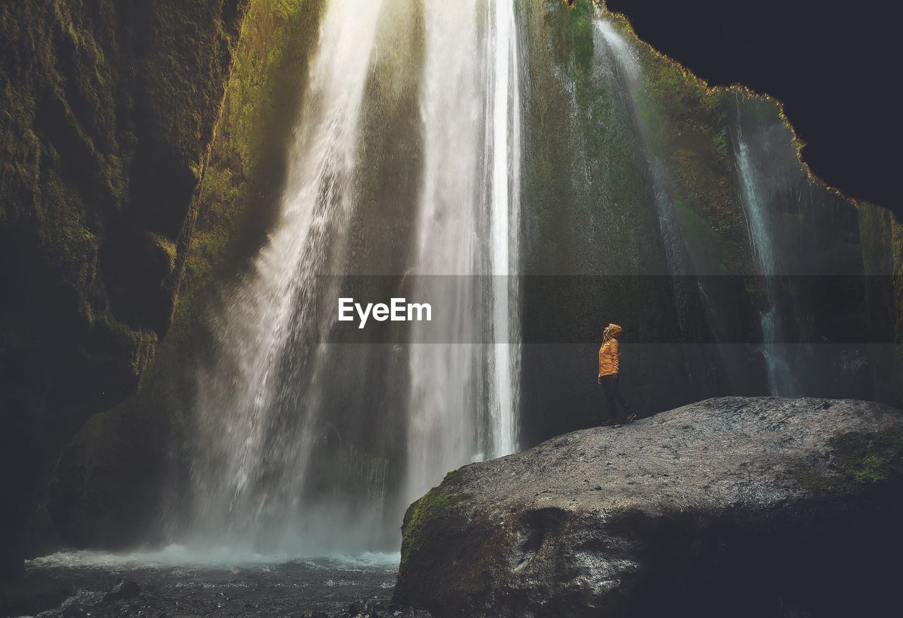 Full length of man standing on rock against waterfall