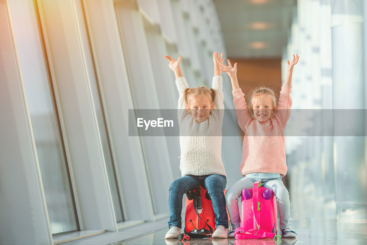 Portrait of cute sisters sitting on luggage at airport