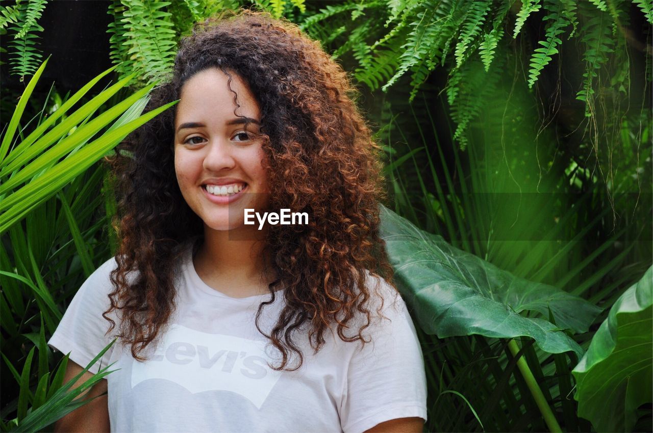Portrait of smiling woman with curly hair against plants