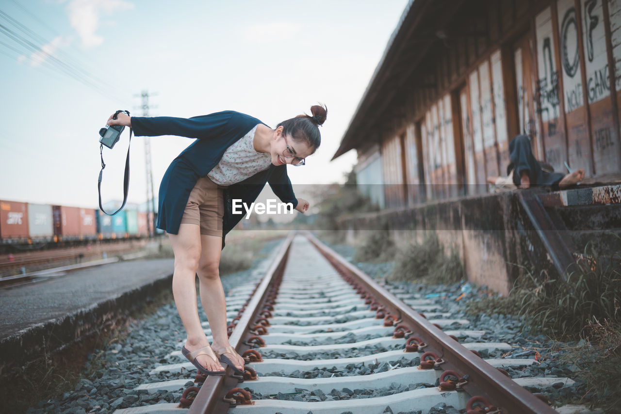 Smiling young woman with camera standing on railroad track