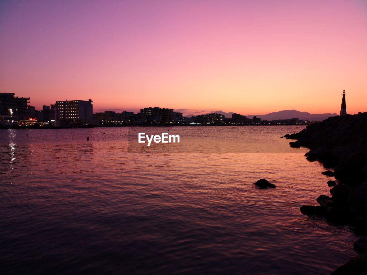 Silhouette city by sea against sky during sunset