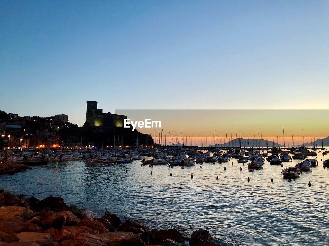 Boats moored at harbor during sunset with a castle 