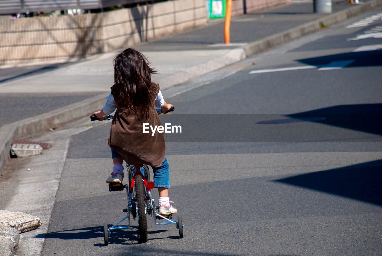 Full length rear view of girl riding bicycle on street