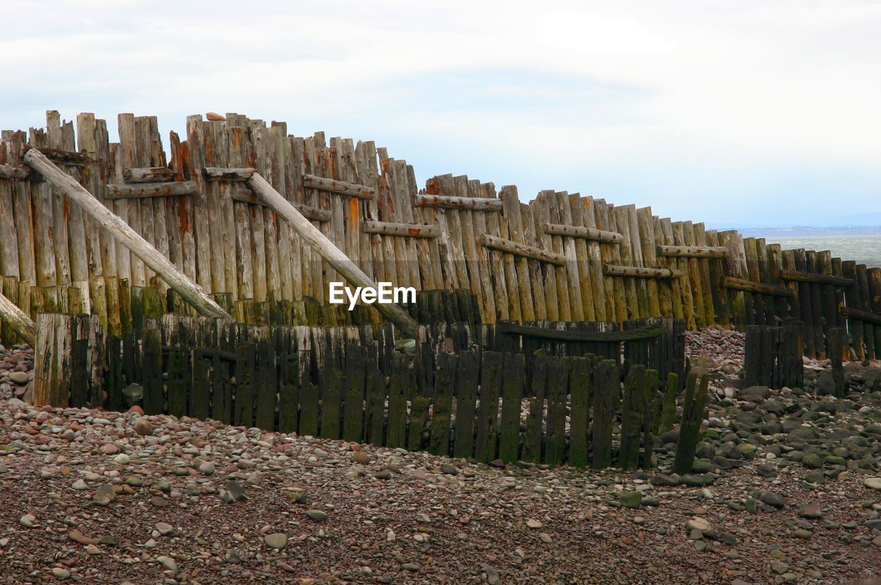 WOODEN POSTS ON BEACH BY SEA AGAINST SKY