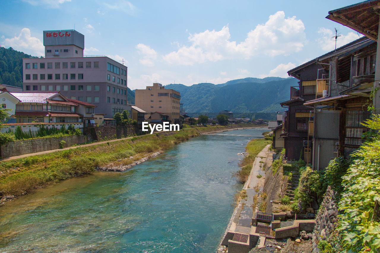 Buildings by river in town against sky