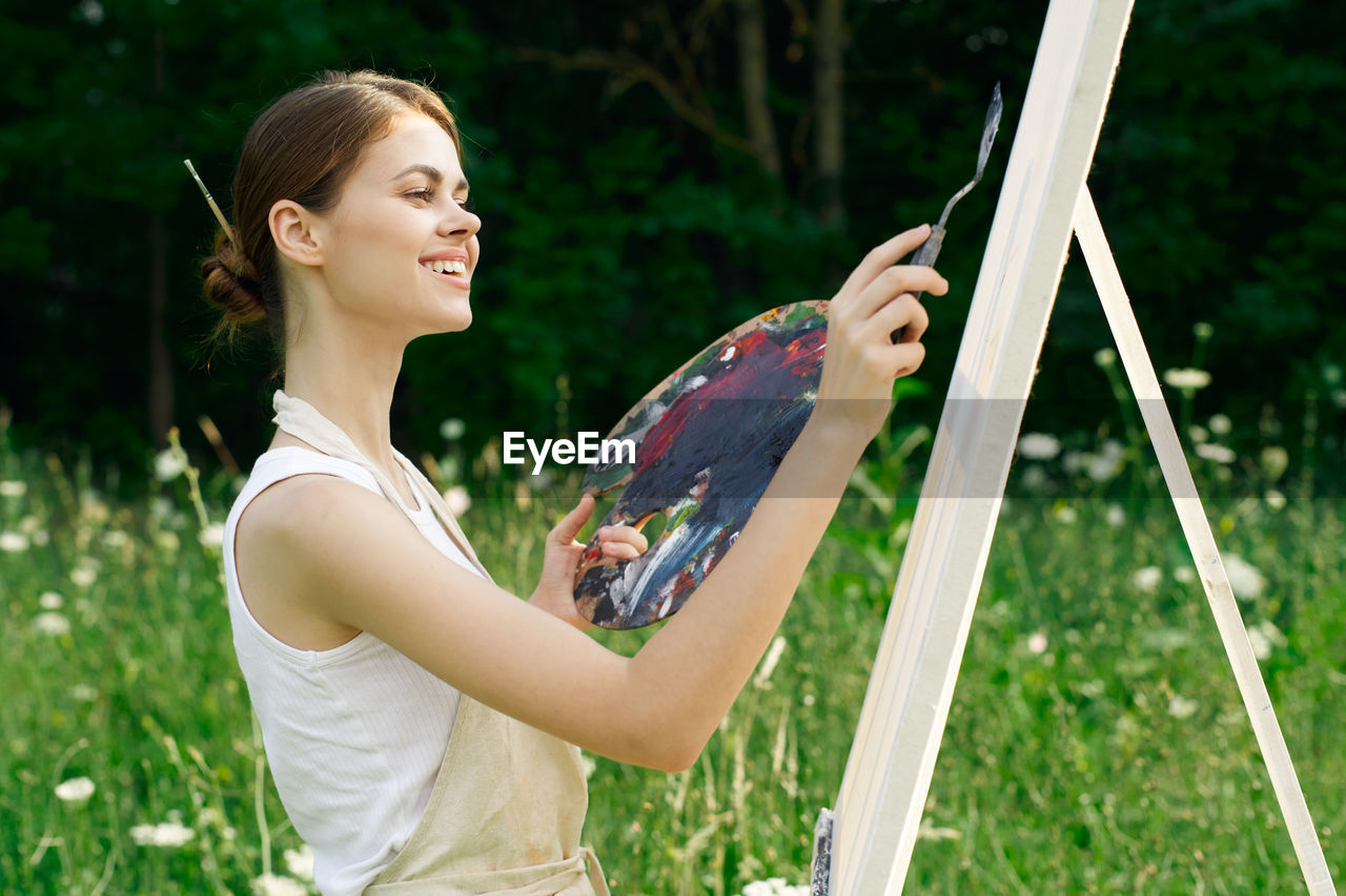 SIDE VIEW OF SMILING YOUNG WOMAN HOLDING PLANT