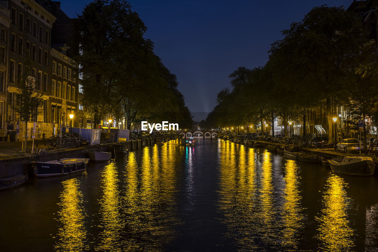 Illuminated city by river against sky at night