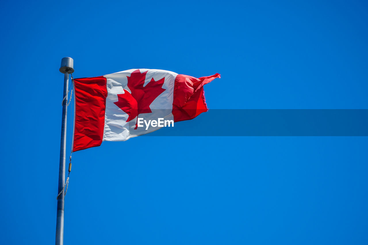 Low angle view of canadian flag waving against blue sky