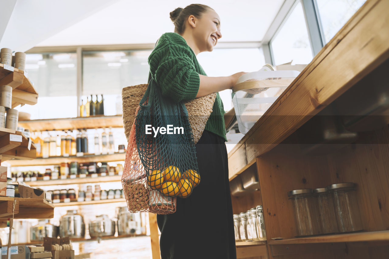 Smiling woman with fruits and groceries in mesh bags at store