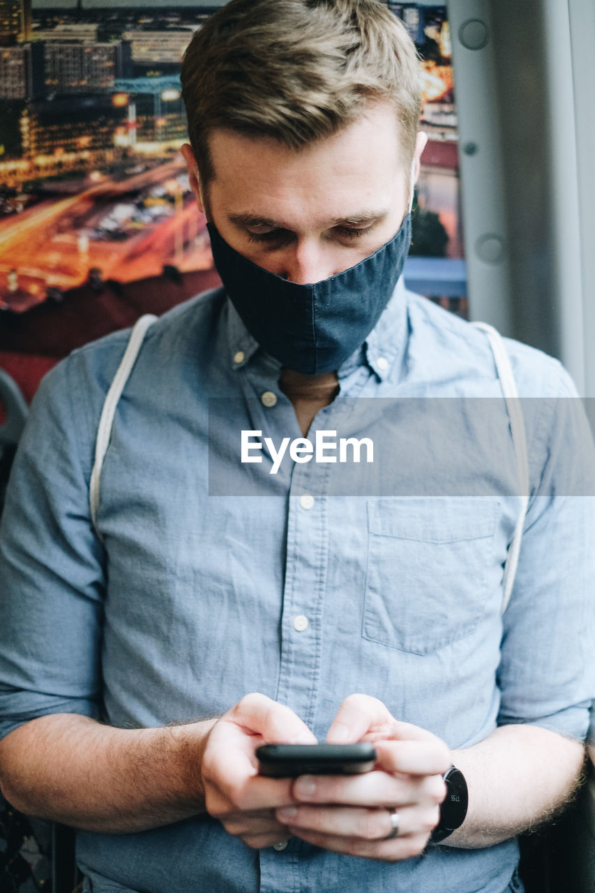 Man wearing mask using mobile phone in train