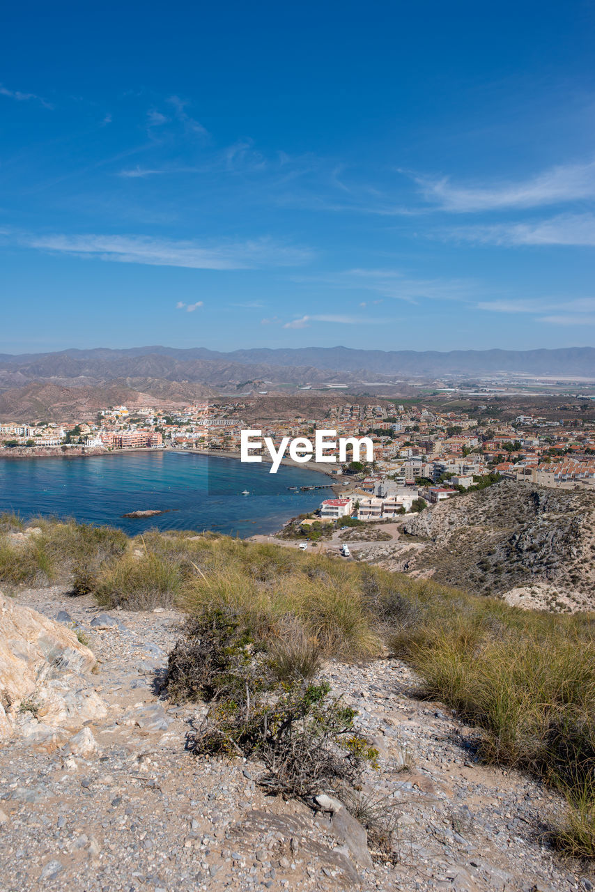 Aerial view of townscape by sea against blue sky