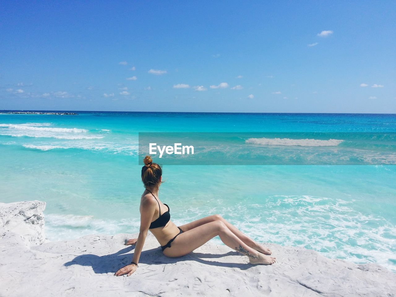 Full length of woman wearing bikini while sitting at beach against blue sky