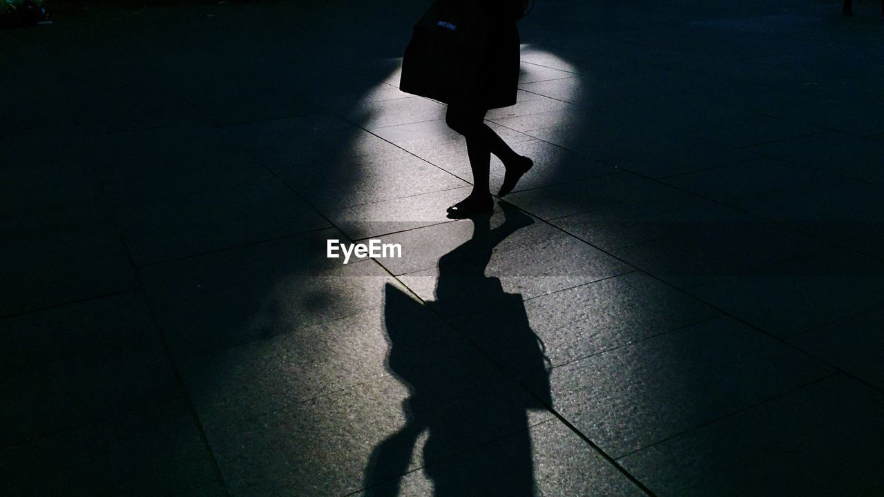 Low section of silhouette woman walking on sidewalk