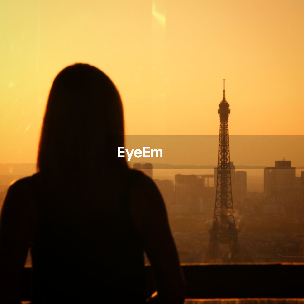 Rear view of silhouette woman looking eiffel tower in city at sunset