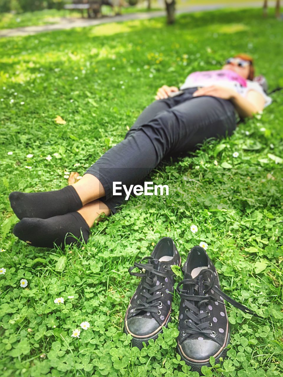 Woman lying by black shoes on grassy field