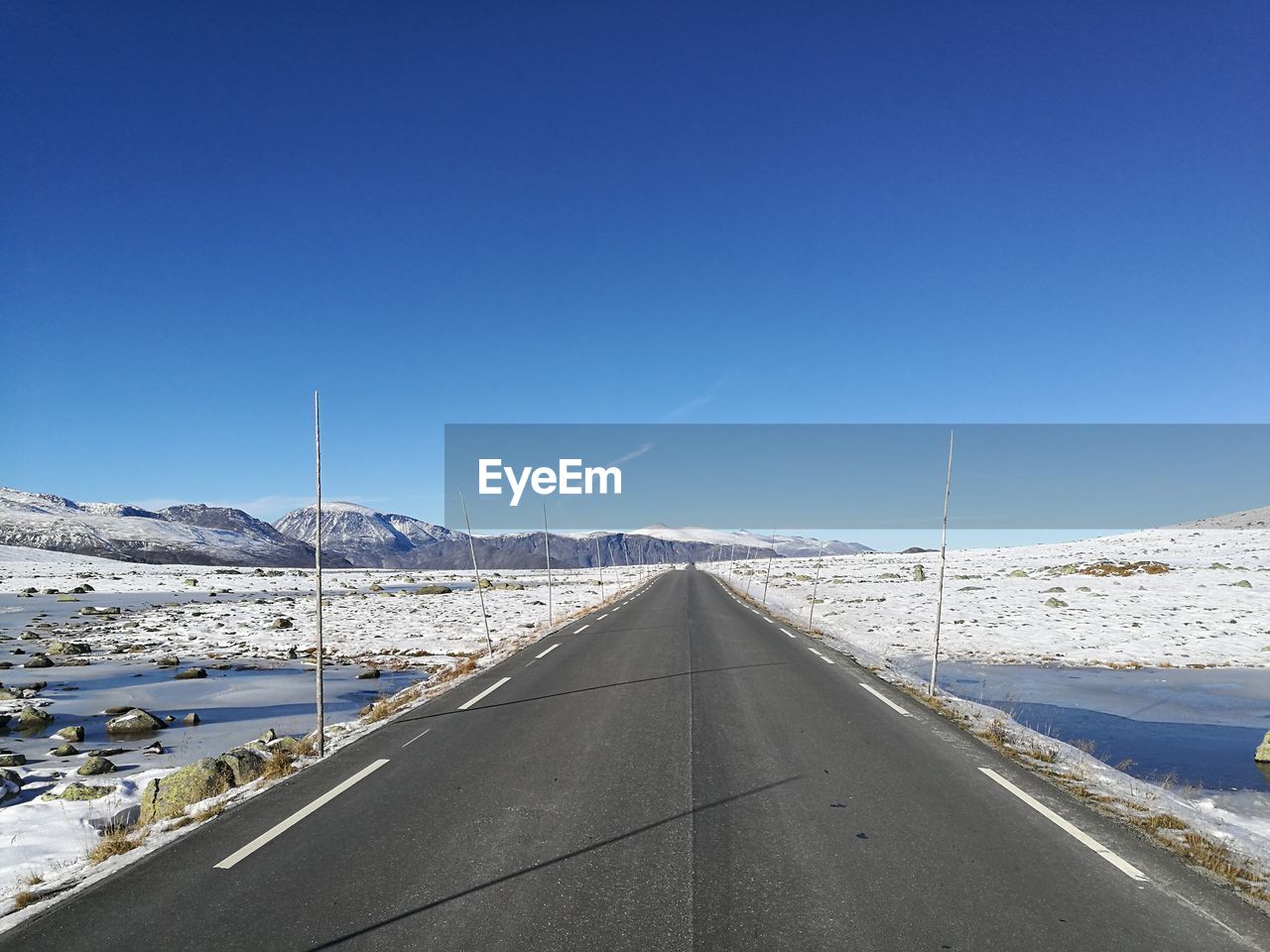 Road amidst snow covered mountains against clear blue sky