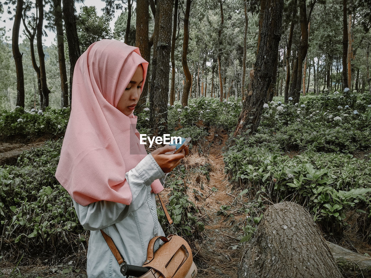 Woman wearing hijab while using mobile phone in forest