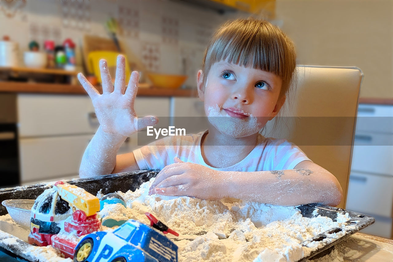 Cute girl plating with toys and flour at home