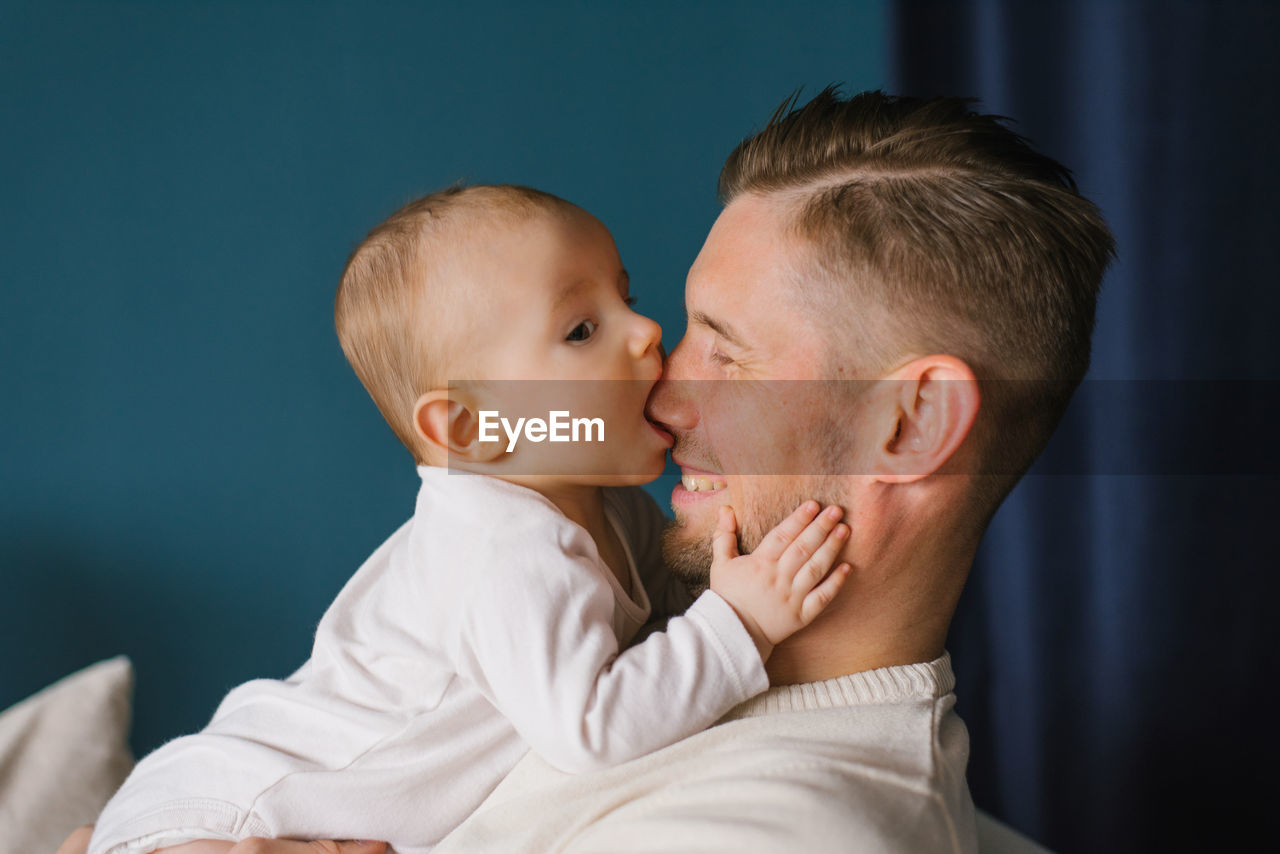 Close-up of a charming 6-month-old caucasian boy biting his dad's nose. the concept of growing teeth