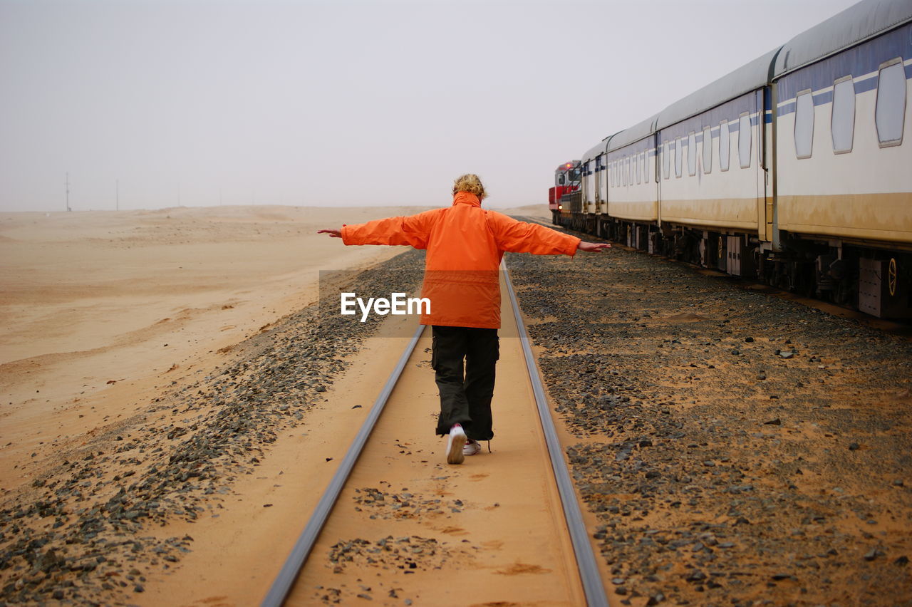 Rear view of woman with arms outstretched on railroad track against sky