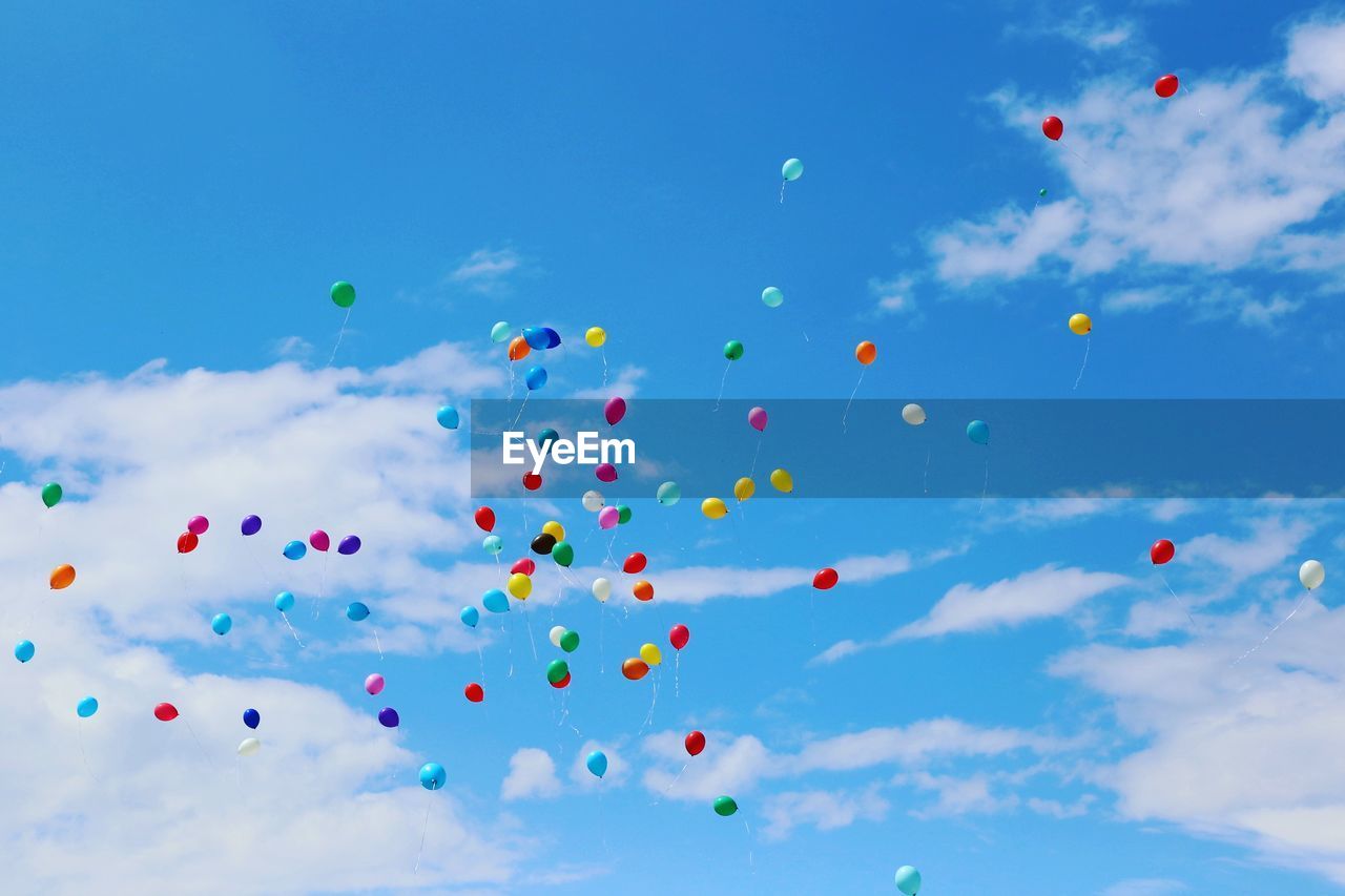 Low angle view of helium balloons flying against blue sky