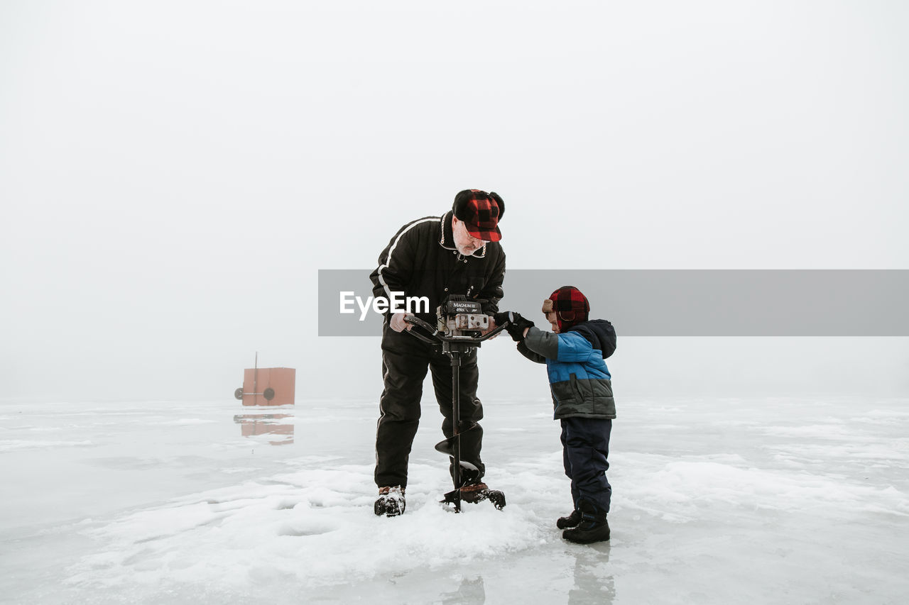 Senior man with grandson using machinery on frozen lake