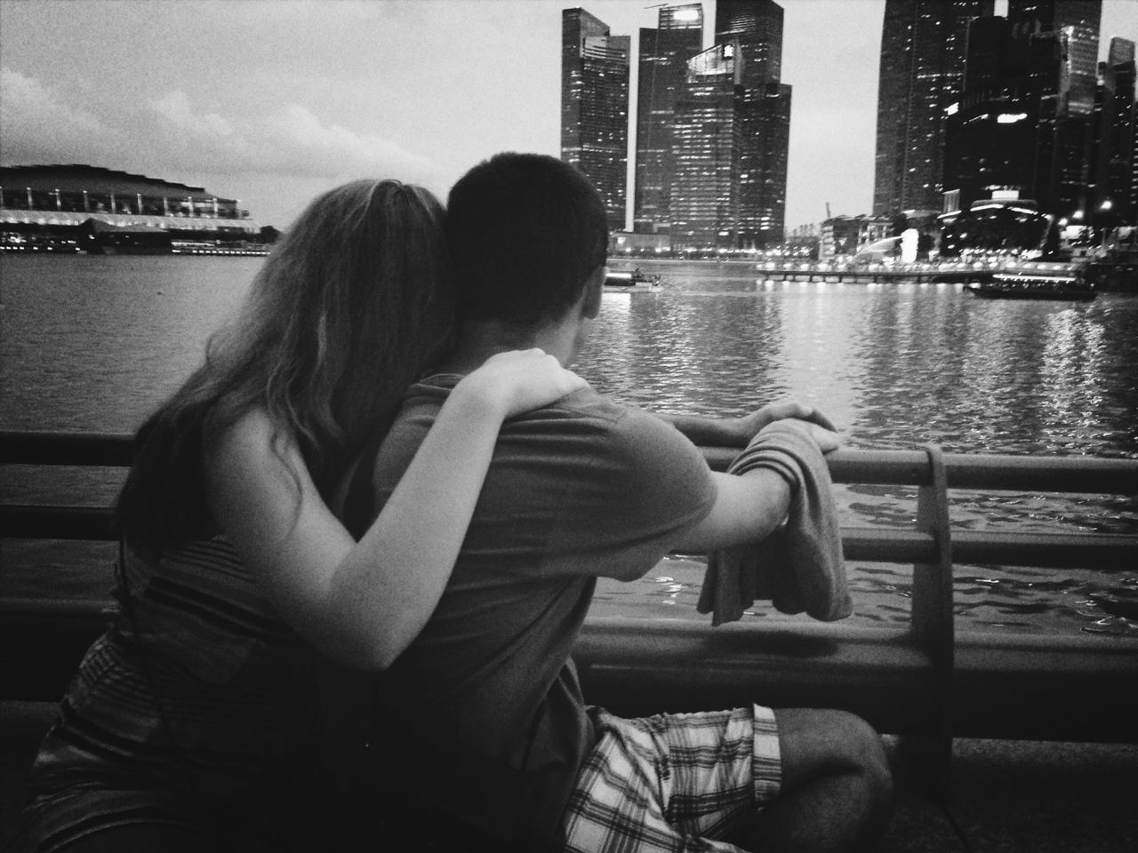 Rear view of couple sitting at railing by sea