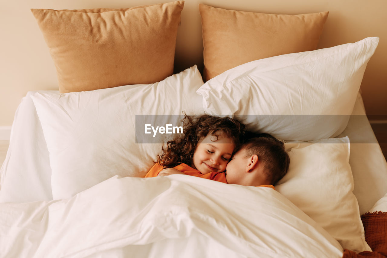 Funny happy kids brother and sister in pajamas playing having fun in a cozy bedroom at home