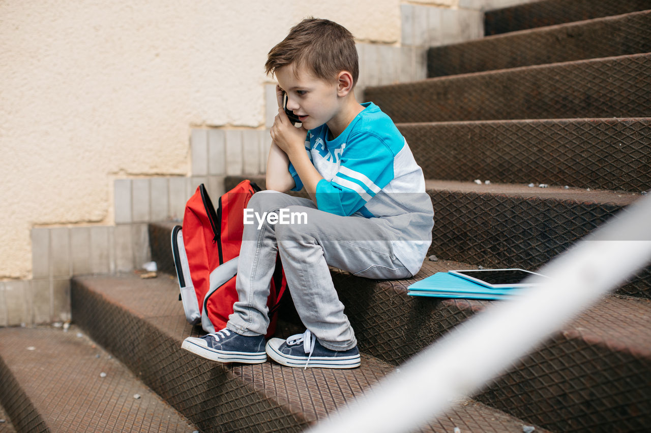 Full length of boy talking on mobile phone while sitting on steps