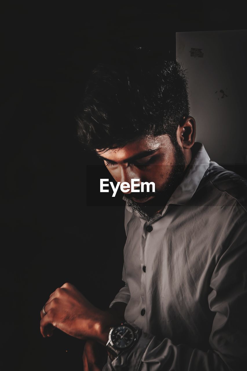 Portrait of young man looking away while standing against black background