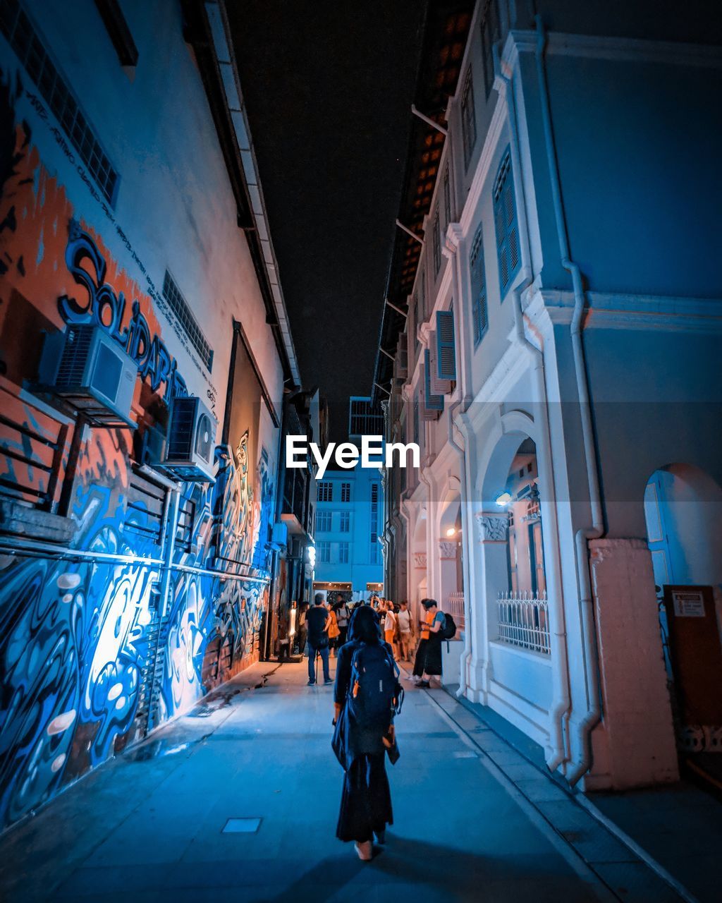 PEOPLE ON ILLUMINATED STREET AMIDST BUILDINGS IN CITY AT NIGHT