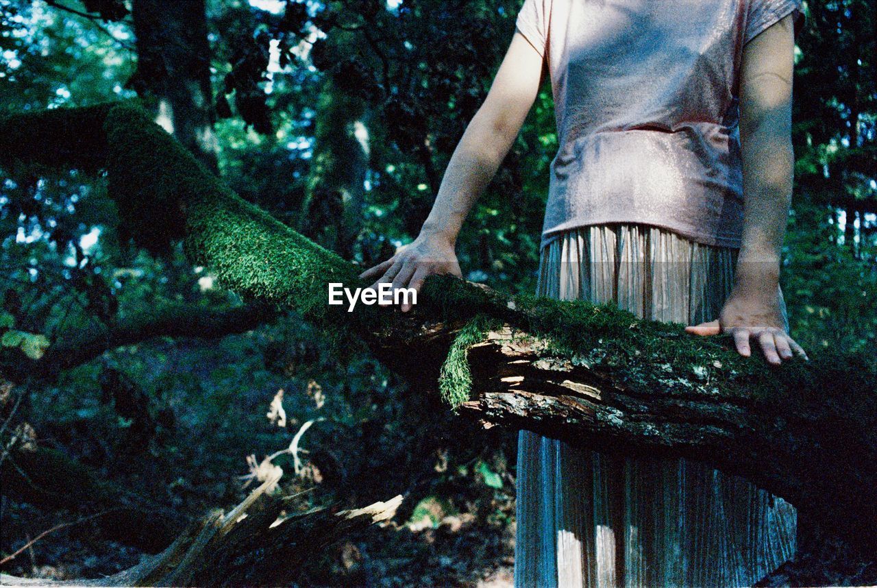 Midsection of pregnant woman standing by tree trunk in forest