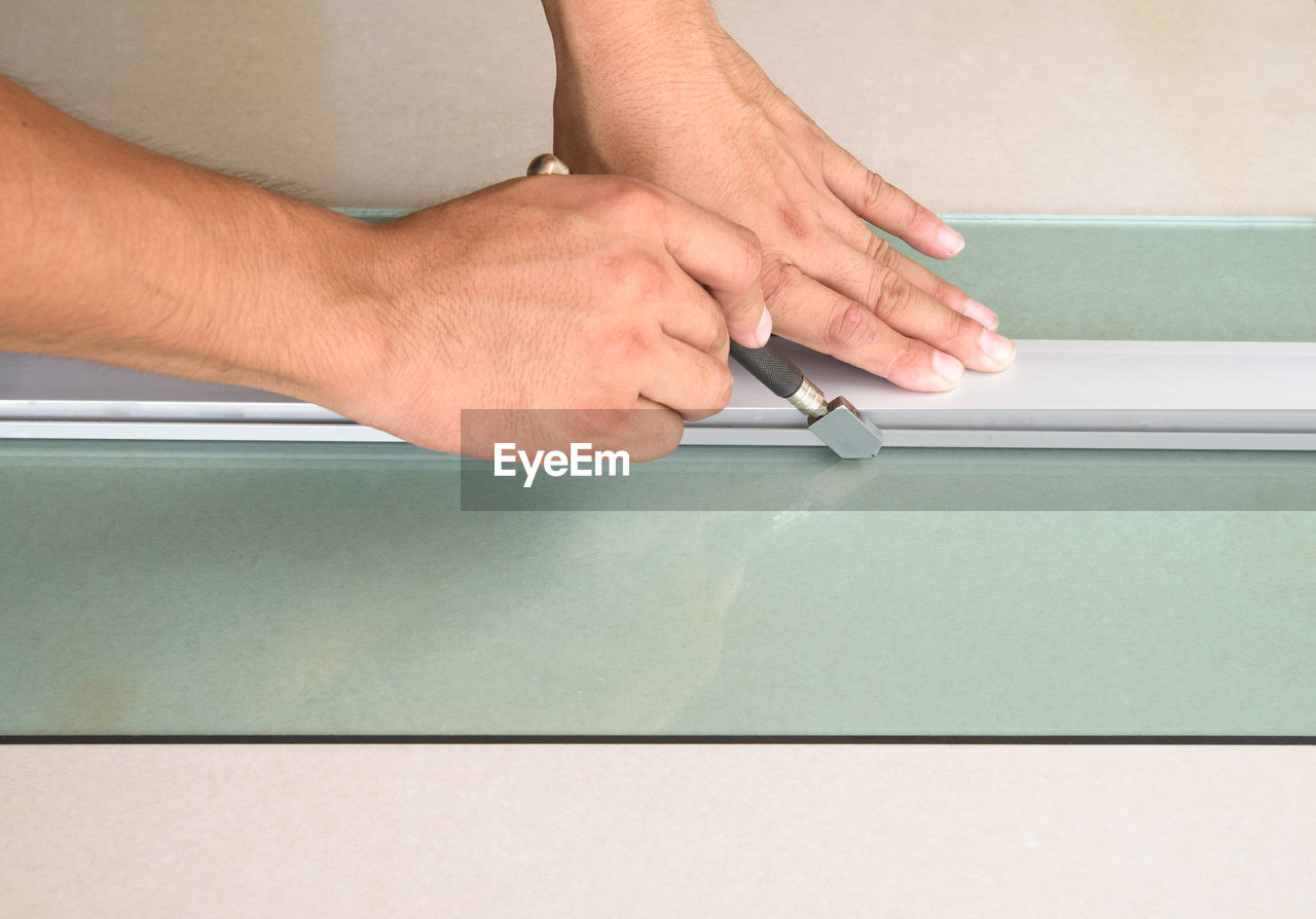 Cropped hands of worker cutting glass on table in workshop