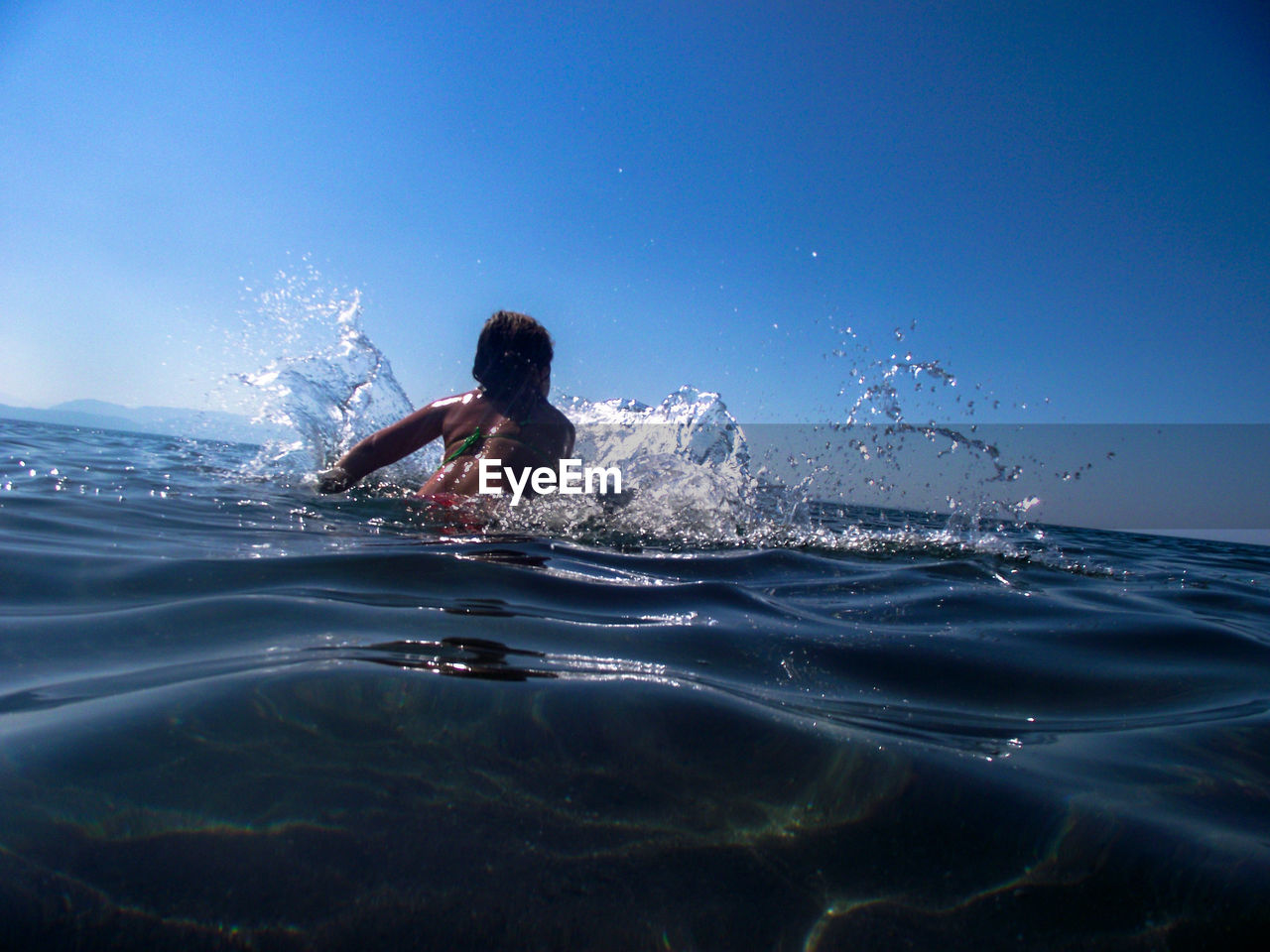 Girl swimming in sea against clear blue sky