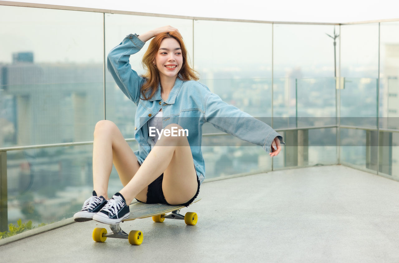 PORTRAIT OF A SMILING YOUNG WOMAN SITTING ON WALL