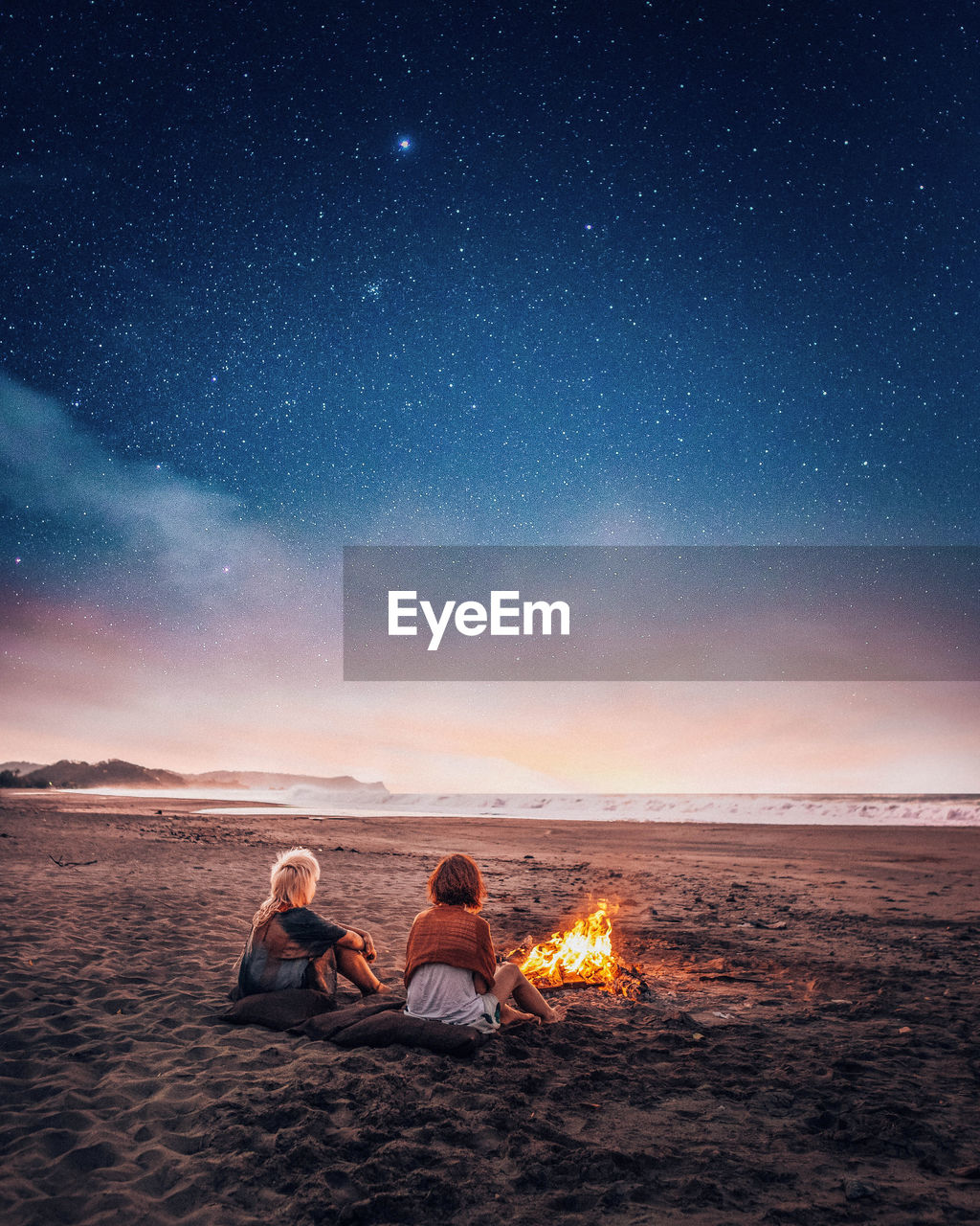 Women sitting by bonfire at beach against sky