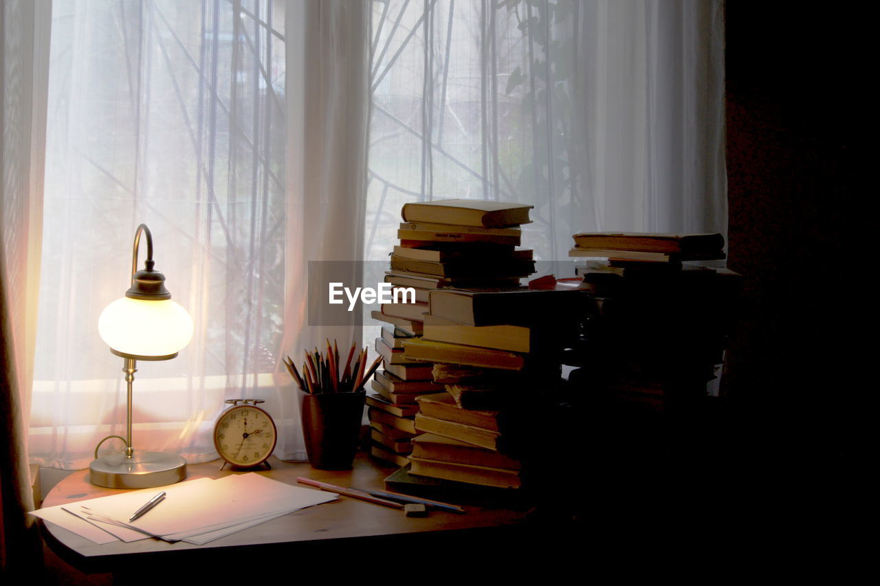 Books and illuminated lamp on desk at home