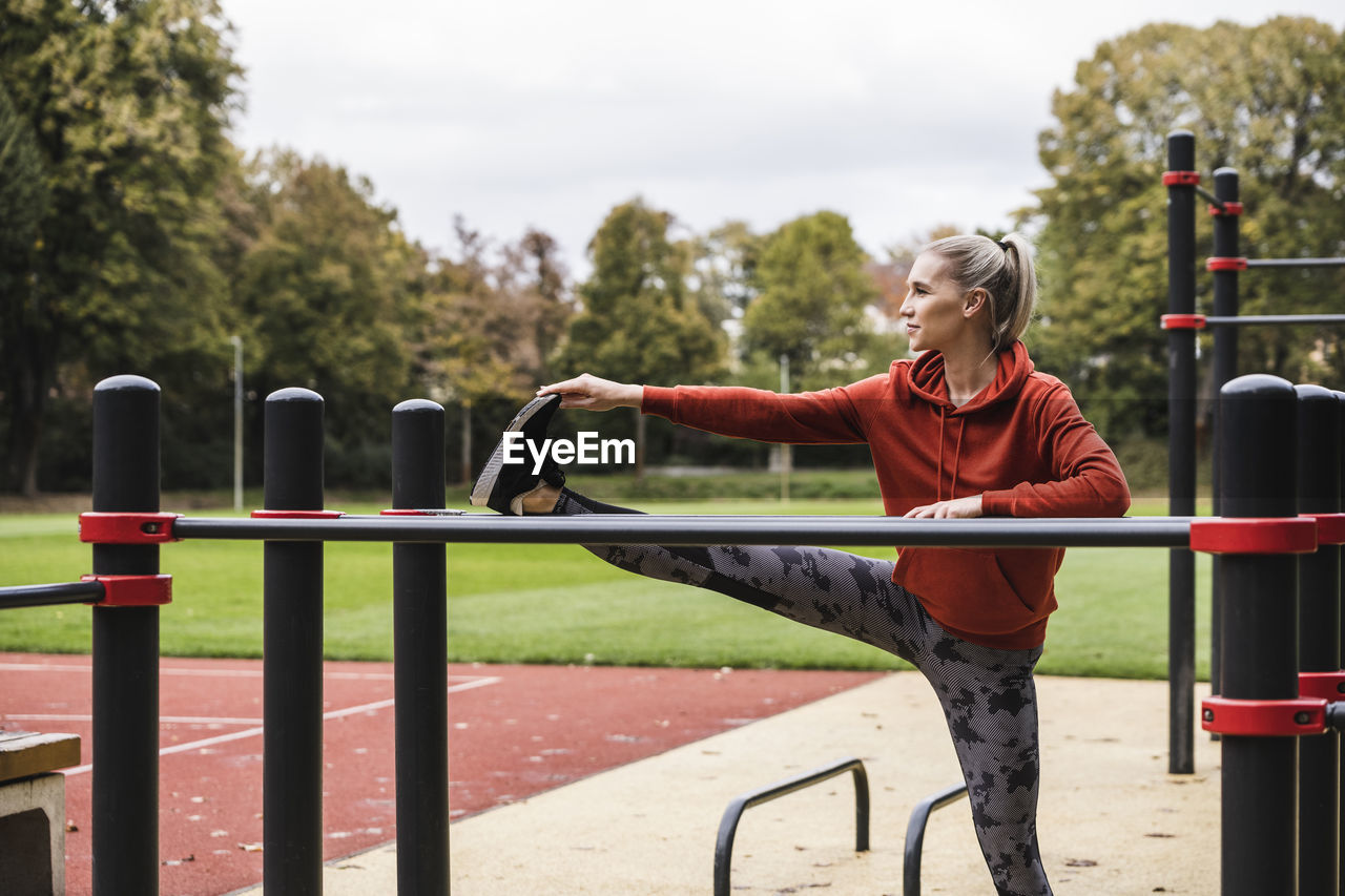 Young sportswoman doing stretching exercise in front of horizontal bar