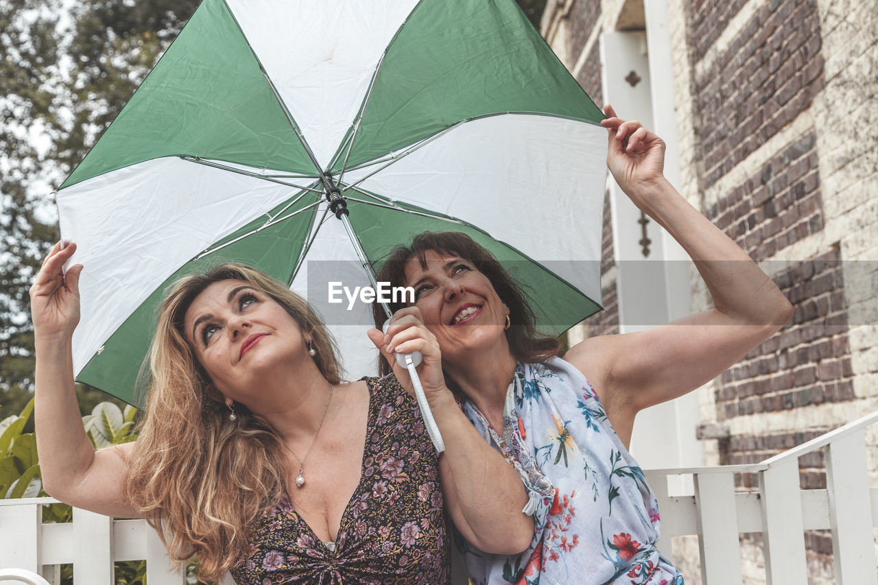 Couple of two attractive fifty year old women with umbrella in front of french villa on a rainy day